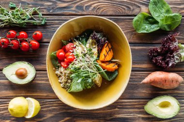 flat lay with vegetarian salad with grilled vegetables, sprouts, cherry tomatoes in bowl and arranged fresh ingredients around on wooden tabletop clipart