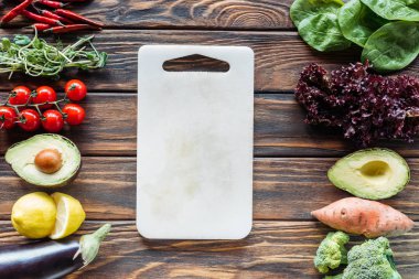 flat lay with empty cutting board and fresh vegetables arranged around on wooden tabletop clipart