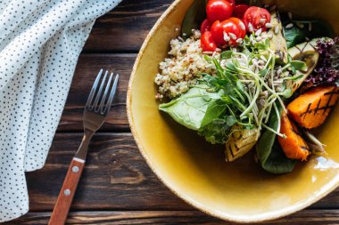 top view of vegetarian salad with grilled vegetables, sprouts, cherry tomatoes in bowl, fork and linen on wooden tabletop clipart