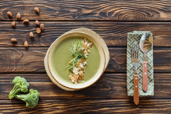 top view of vegetarian cream soup with broccoli, sprouts and almonds in bowl on wooden tabletop