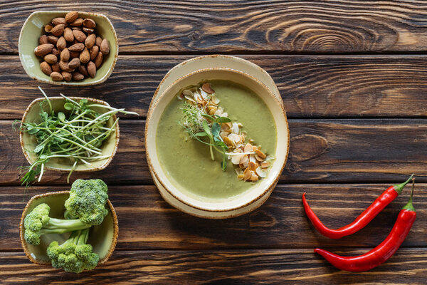 top view of arranged vegetarian cream soup, sprouts, almonds and fresh broccoli in bowls on wooden surface