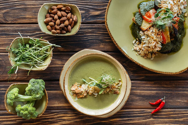 плоский укладка с расположением вегетарианский салат, крем суп и ингредиенты вокруг на деревянной поверхности
