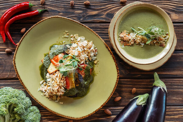 плоский укладка с расположением вегетарианский салат, крем суп и ингредиенты вокруг на деревянной поверхности
