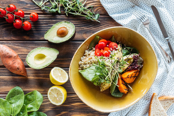 flat lay with vegetarian salad with grilled vegetables and sprouts, linen and cutlery on wooden surface