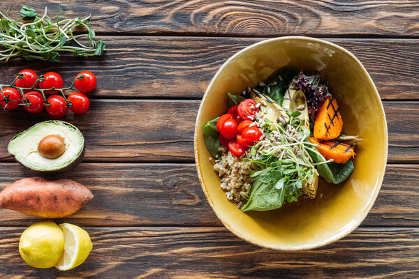 flat lay with vegetarian salad with grilled vegetables, sprouts, cherry tomatoes in bowl and arranged fresh ingredients around on wooden tabletop