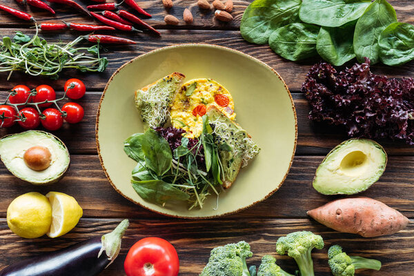 flat lay with vegetarian salad served on plate and fresh ingredients arranged around on wooden tabletop