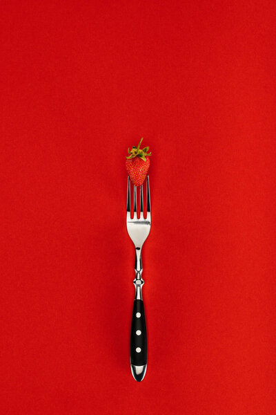 Red strawberry on a fork isolated on red background