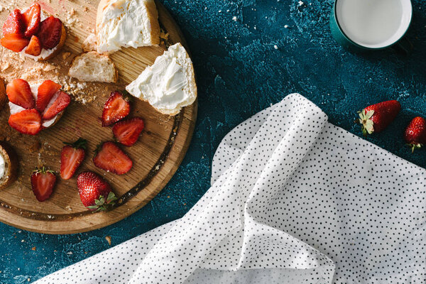 Wooden board with strawberry sandwiches in mess on blue table with tablecloth