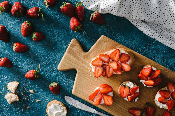 top view of bread with cream cheese and strawberries on wooden cutting board