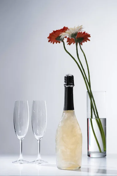在灰色背景下 关闭空眼镜 香槟瓶和非洲菊花束的全景图 — 免费的图库照片
