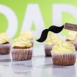 Cupcakes cremosos com sinal de bigode e inscrição feliz dia dos pais na frente da inscrição do pai feito de letras brancas em verde