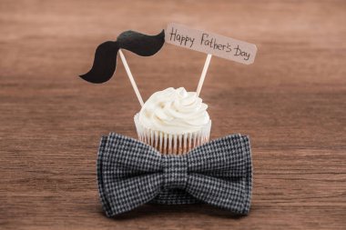 tasty cupcake with mustache sign, bowtie and Happy fathers day inscription on wooden surface clipart