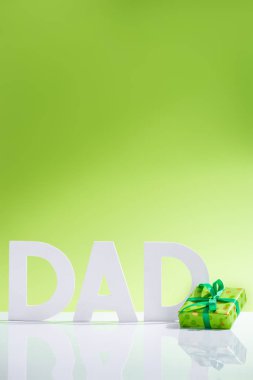 green gift box in front of dad inscription made of white letters on green, Happy fathers day concept clipart