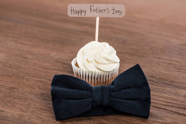 tasty cupcake with bowtie and Happy fathers day inscription on wooden surface