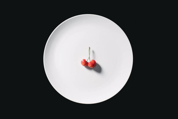 верхний вид свежих спелых сладких желтых вишен на круглой белой пластине изолированы на черном
