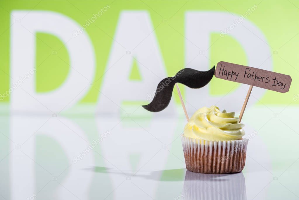 creamy cupcake with mustache sign and Happy fathers day inscription in front of dad inscription made of white letters on green