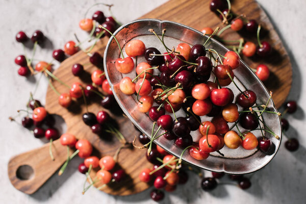 top view of sweet ripe cherries on vintage plate and wooden cutting board on white, selective focus