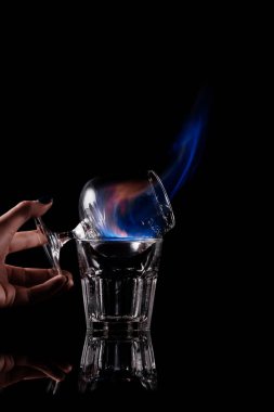 partial view of woman holding glass with burning sambuca alcohol drink on black background clipart