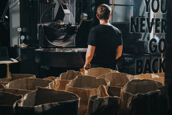Man standing by paper bags with coffee beans in industrial coffee shop