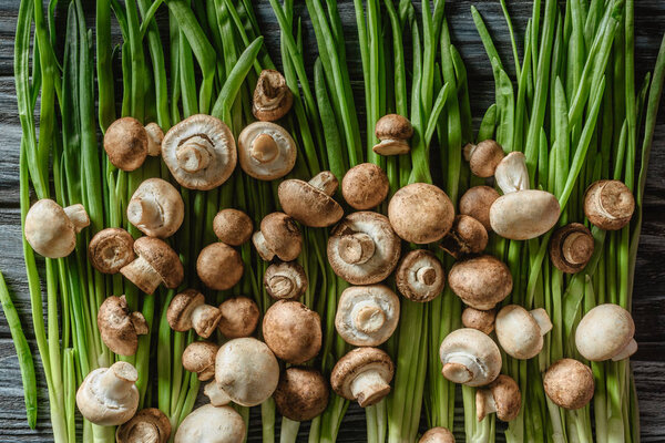 top view of raw champignon mushrooms on green leeks on wooden tabletop