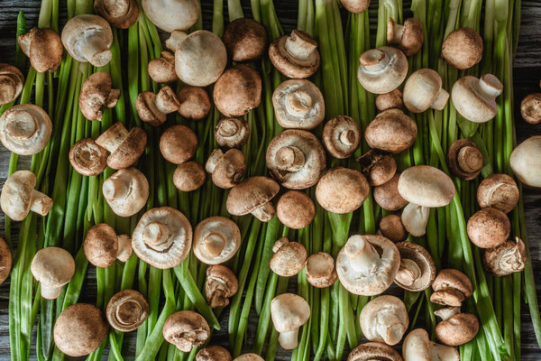 top view of champignon mushrooms on green leeks on wooden tabletop