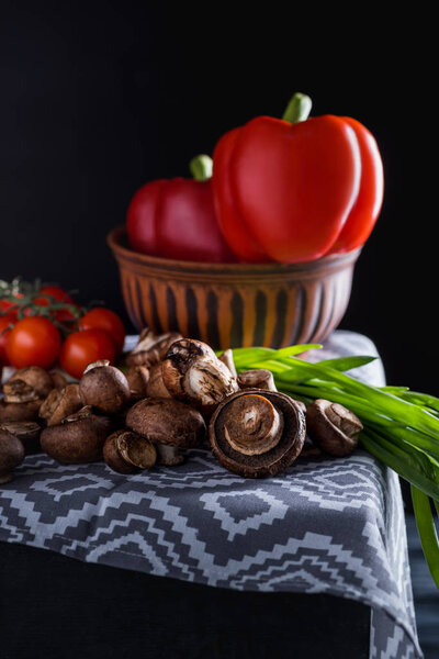 close-up shot of raw champignon mushrooms with vegetables on blue napkin on black