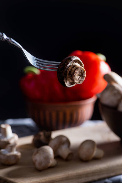 close-up shot of champignon mushroom pierced with fork on dark blurred background