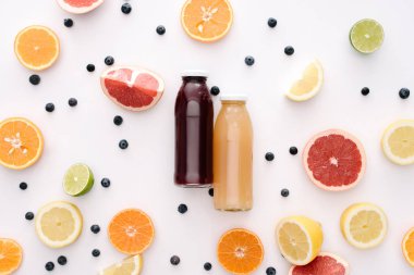 top view of glass bottles of fresh juice with citrus fruits slices on white surface clipart