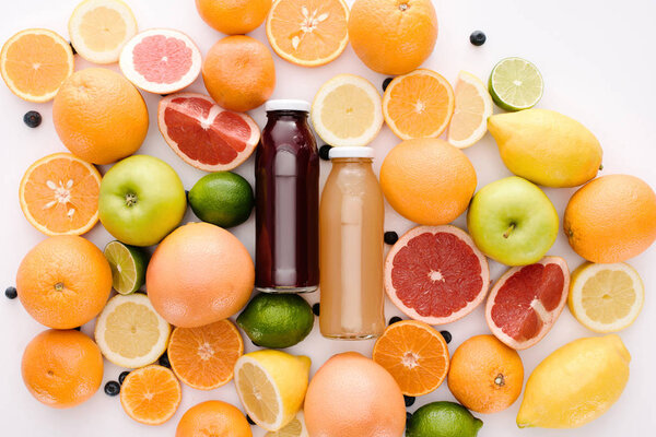 top view of bottles of fresh juice with ripe citrus fruits slices on white surface