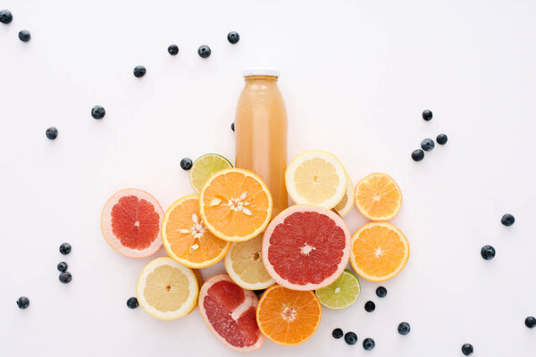 top view of bottle of juice with citrus fruits slices and blueberries on white surface