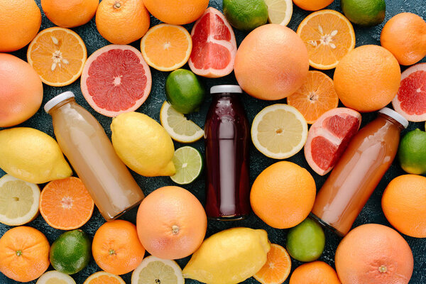 top view of glass bottle of fresh juice surrounded with citrus fruits slices on blue concrete surface