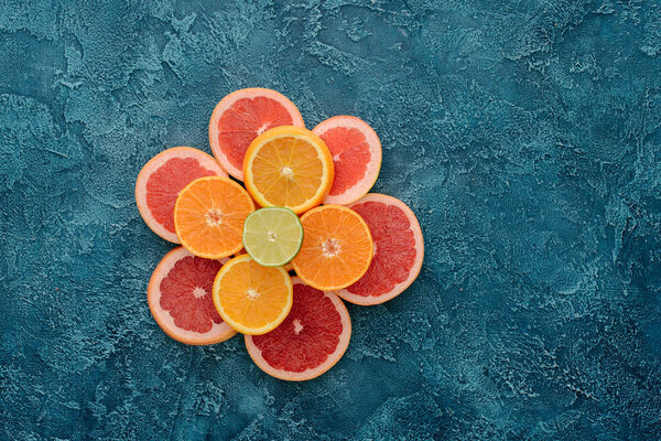 top view of stacked various citrus fruits slices on blue concrete surface