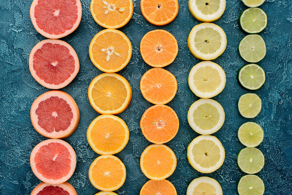 top view of citrus fruits slices in rows on blue concrete surface