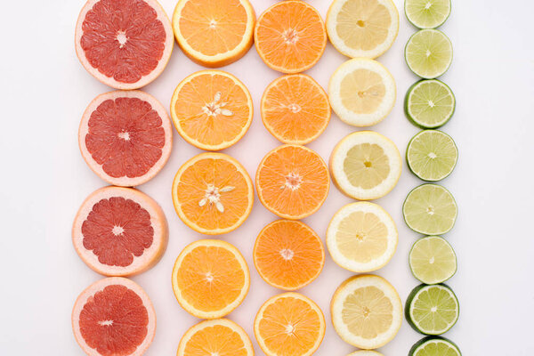 top view of various citrus fruits slices in rows on white surface