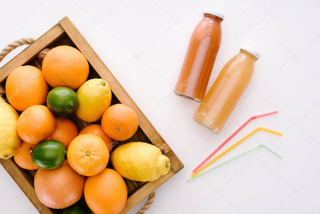 top view of various citrus fruits with bottles of juice on white tabletop