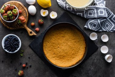 düz lay pasta hamuru, kase ve koyu gri masa üzerinde taze çilek kremi ile
