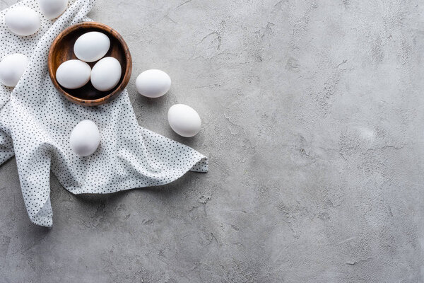 flat lay with raw chicken eggs in bowl and linen on grey tabletop