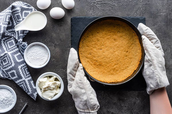 обрезанный снимок женщины в духовке, держащей форму выпечки с тестом в руках на темно-серой столешнице
