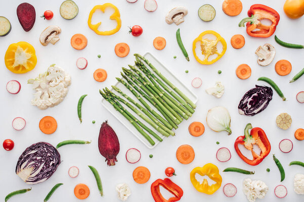 top view of fresh green asparagus on plate and fresh sliced vegetables isolated on white 