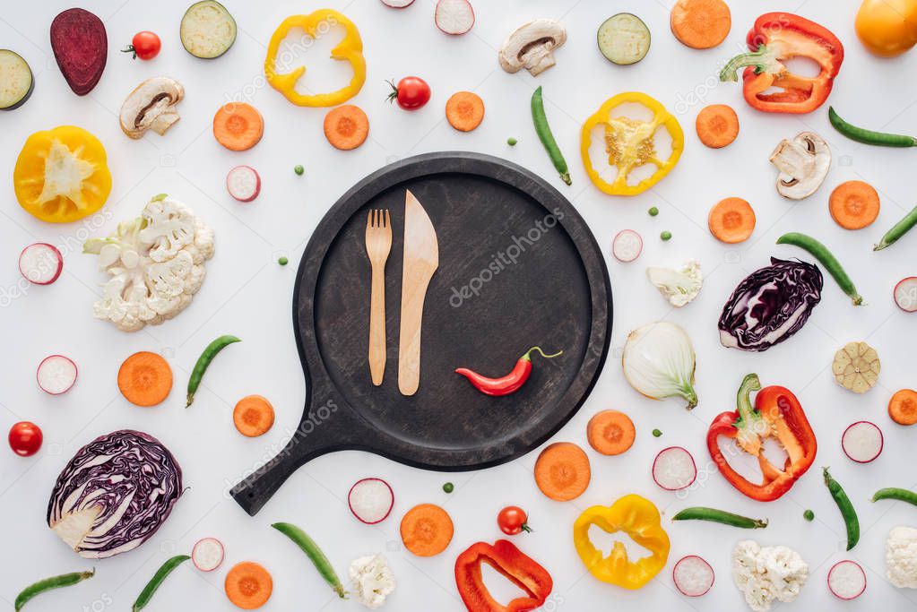 top view of fork, knife and chili pepper on round wooden board isolated on white 