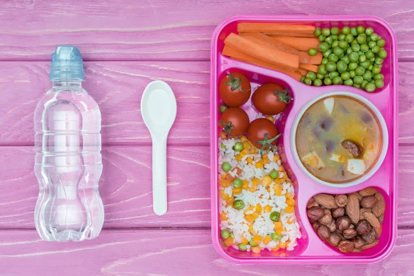 顶部视图的托盘与孩子的午餐学校和瓶水在粉红色的桌子上 — 图库照片