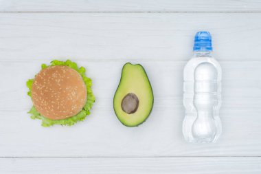 üstten görünüm Burger, avokado ve plastik şişe su ahşap tablo