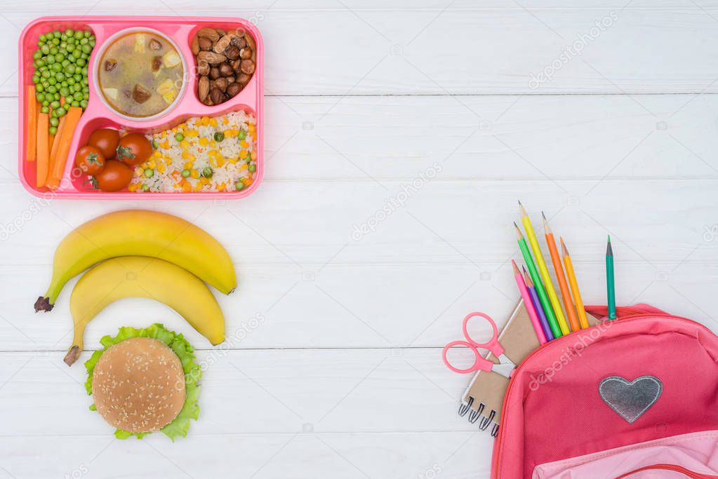 top view of tray with kids lunch, school bag with colored pencils on white wooden table