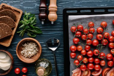 Pan with cherry tomatoes on dark wooden table by bread and herbs clipart