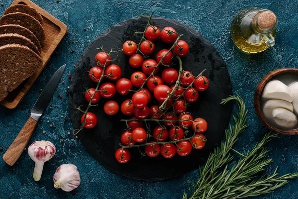 Dark slate board with red tomatoes on blue table with bread and condiments — Stock Image Dark Slate Board Red Tomatoes Blue Table Bread Condiments Stock Picture