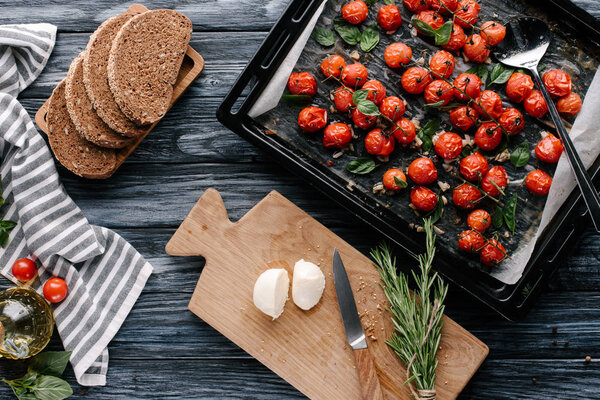 Pan with baked tomatoes and pieces of cheese and bread on dark wooden table