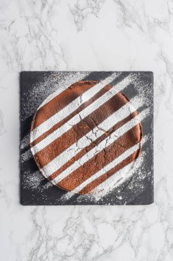top view of delicious homemade cake with icing on slate board on marble surface clipart