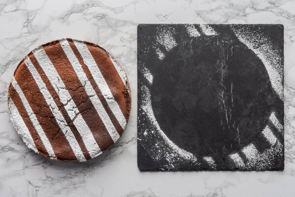 top view of delicious homemade cake and slate board with sugar powder on marble surface