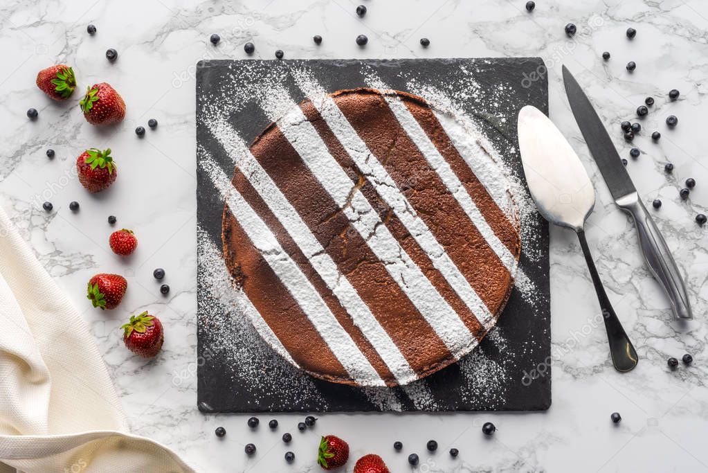 top view of delicious homemade brown cake with frosting and fresh berries on marble surface  