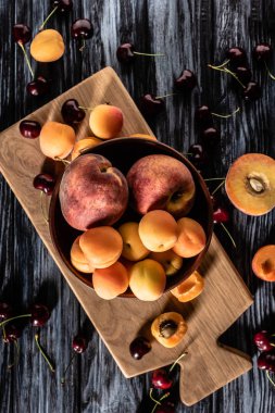 elevated view of bowl with apricots and peaches surrounded by cherries on wooden talbe  clipart